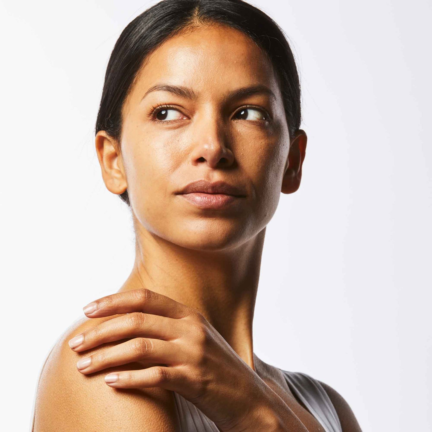 Close up of woman with glowing skin touching her shoulder.
