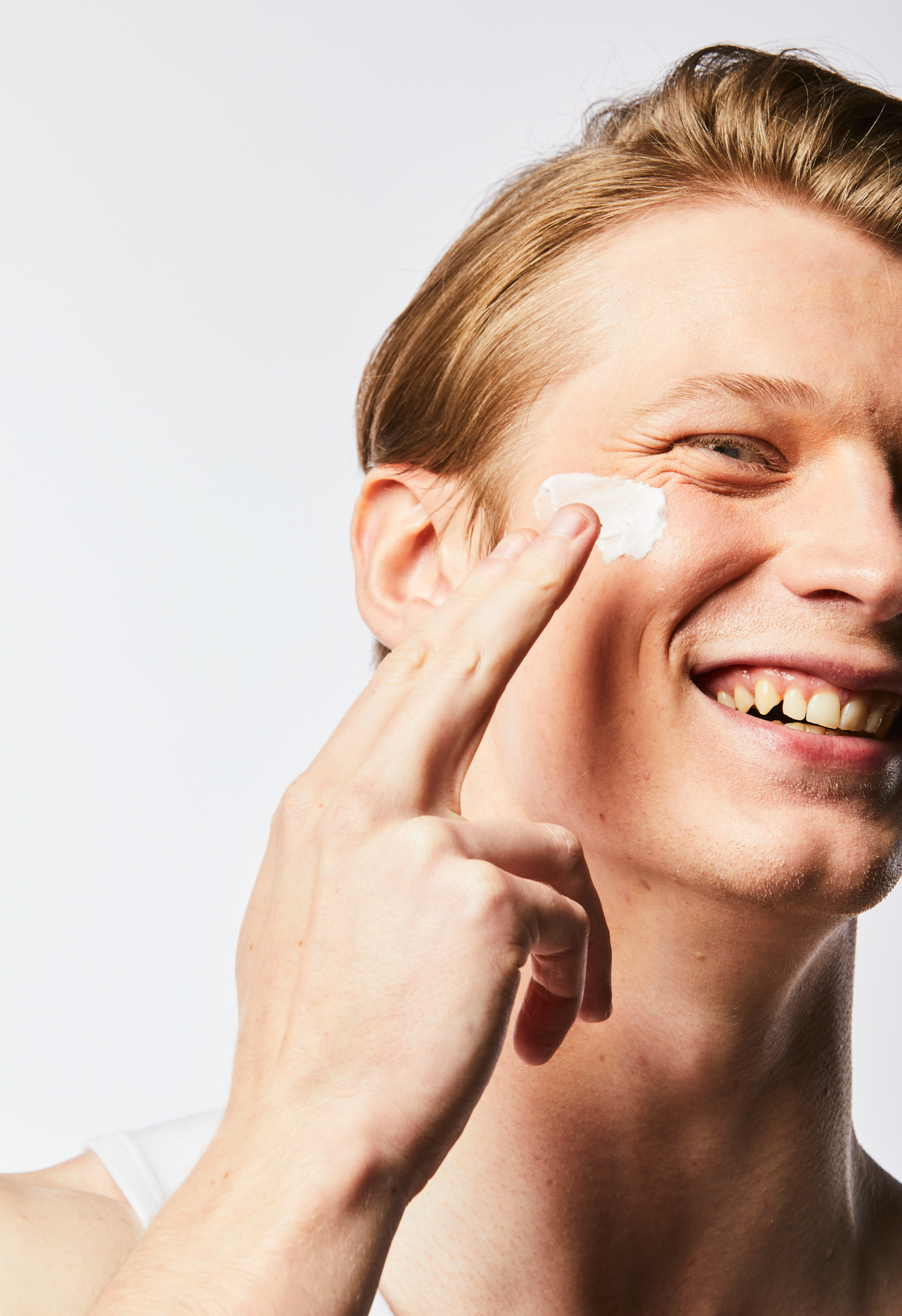 Close up of the right side of a model's face as he applies Calm Cream to his cheek.