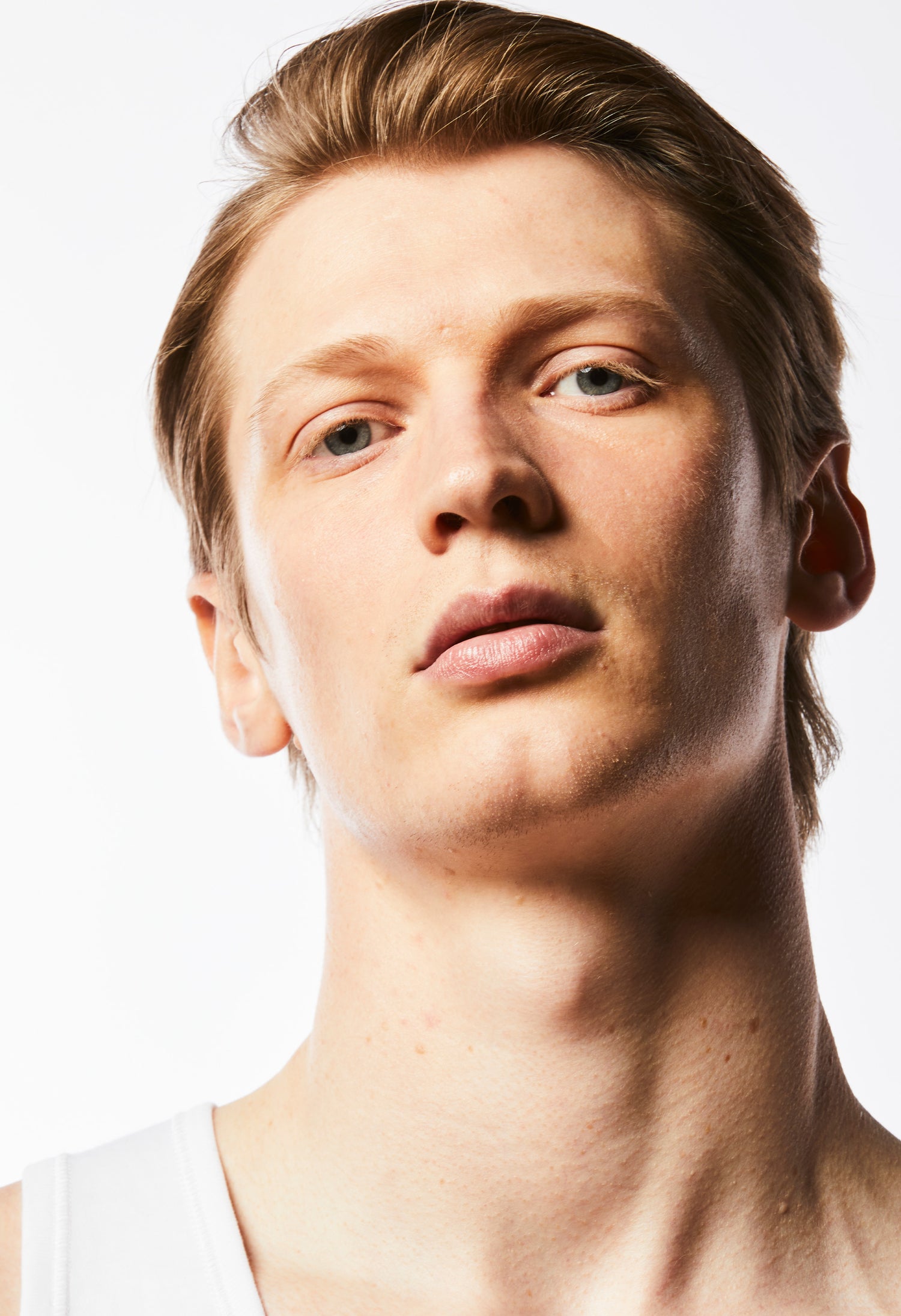 A close up headshot of a model with clear skin tilting his head to the site with shadows across the left side of his face.