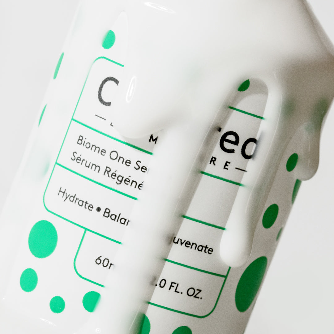 Close up of a white bottle with green spots with Biome One Serum running down the front.