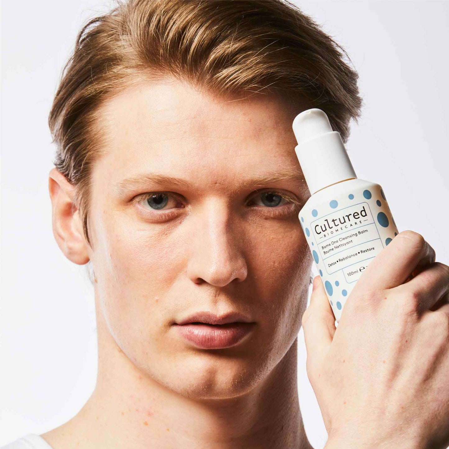 A close up headshot of a man holding the Biome One Cleansing Balm up to his face.