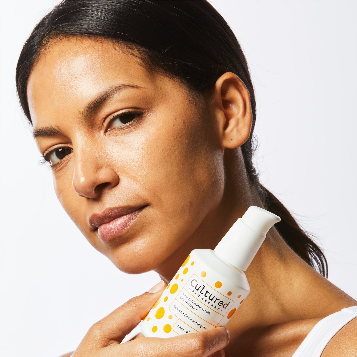 A close up headshot of a woman holding the Cleansing Milk next to her face.