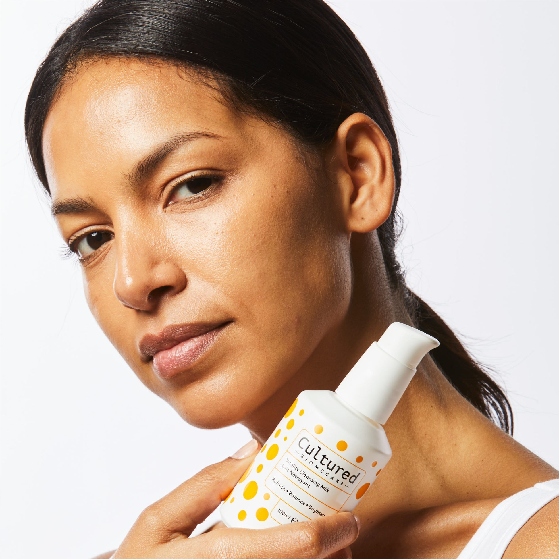 A close up headshot of a woman holding the Cleansing Milk next to her face.