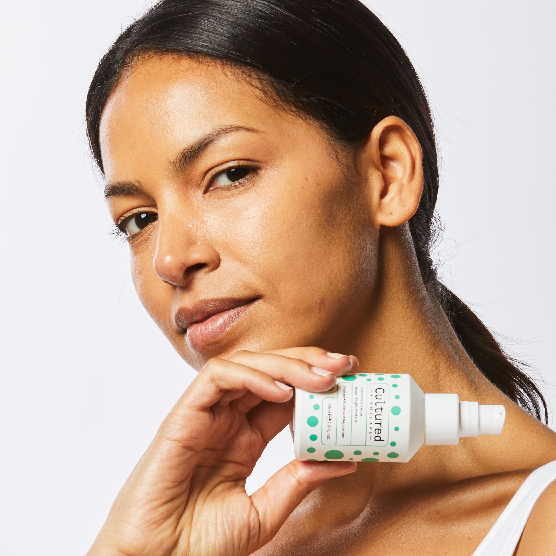 A close up headshot of a woman holding the Biome One Serum.